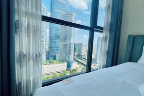 A hotel room with a large window offering a view of modern high-rise buildings and a cityscape.
