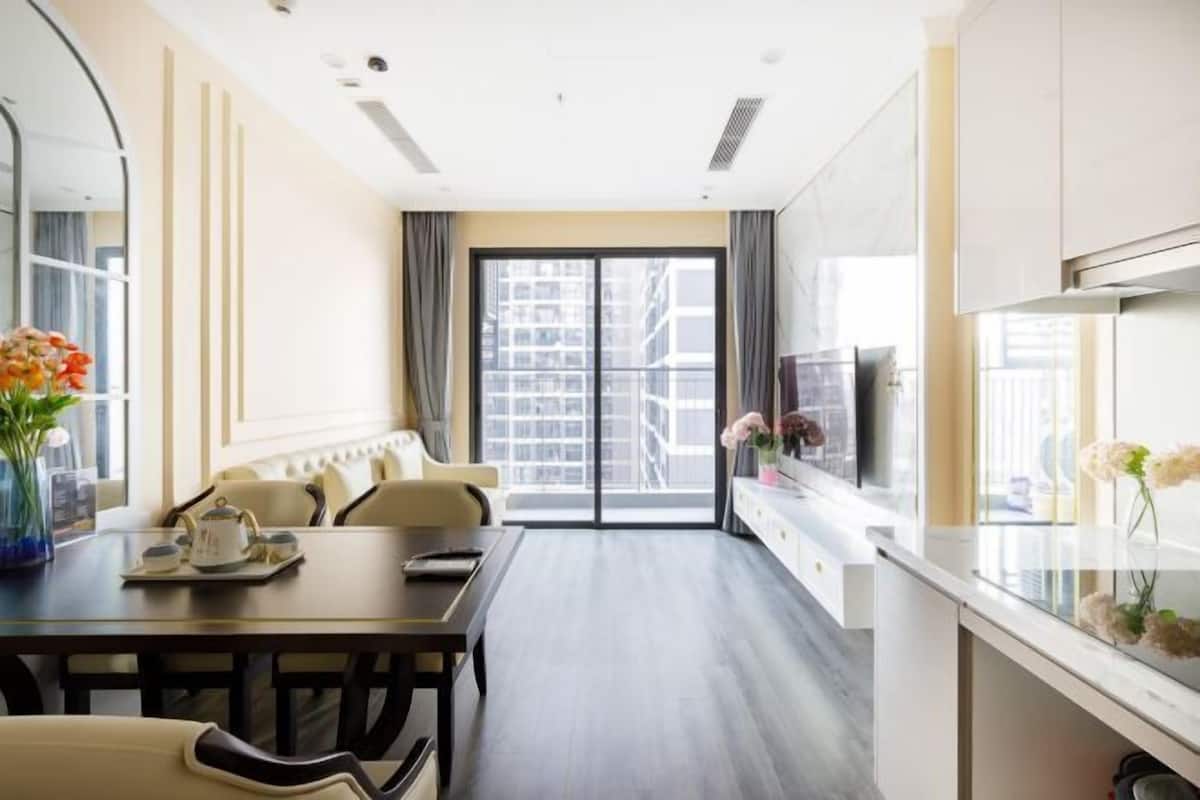 Quarto de hotel com área de refeições, sofá, televisão e uma grande janela com vista para a cidade.