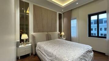 A modern bedroom with a large bed, bedside tables, a mirror, and a window with a view.