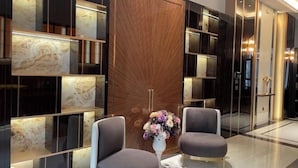 Eine moderne Lobby mit Marmorwand, einem Holzschrank und zwei grauen Sessel.