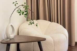A plush armchair with a vase and a glass on a small table. - AA Luxury Housing (Hanoi)