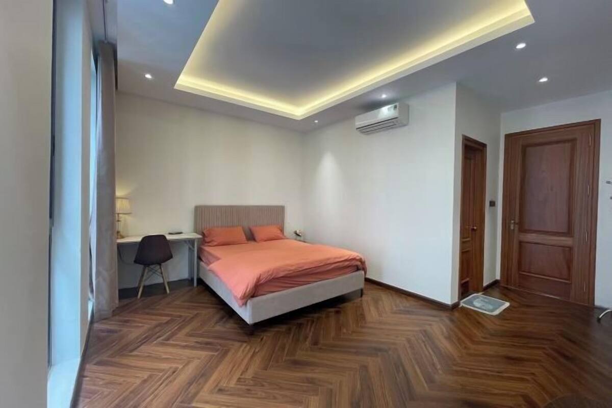 Een slaapkamer met een bed, bureau, stoel en houten vloeren.