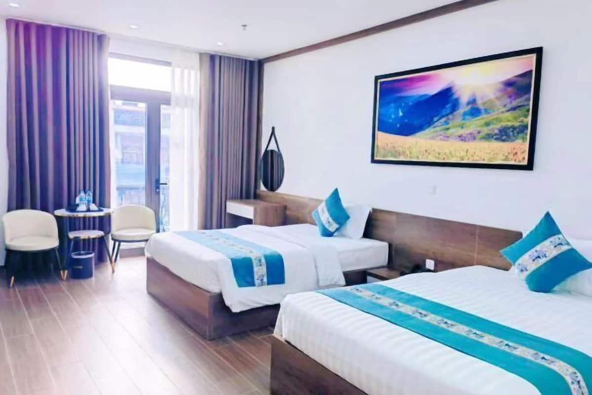 A hotel room with two beds, a desk, a chair, and a large window.