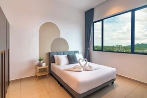 A modern hotel room with a large bed, a small bedside table, a potted plant, and a view of the cityscape through a large window.