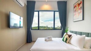 Quarto de hotel com cama, televisão de tela plana na parede, janela com cortinas e um cartaz na parede.