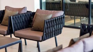 Uma área de estar com cadeiras e bancos estofados, disposta em um ambiente interno moderno.