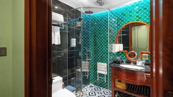 Casa de banho com chuveiro em vidro, lavatório com espelho e chão estampado.