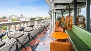 Une terrasse sur le toit offrant une vue sur les toits de la ville, aménagée avec différents types de sièges, notamment des tabourets de bar et un banc rembourré de couleur verte.