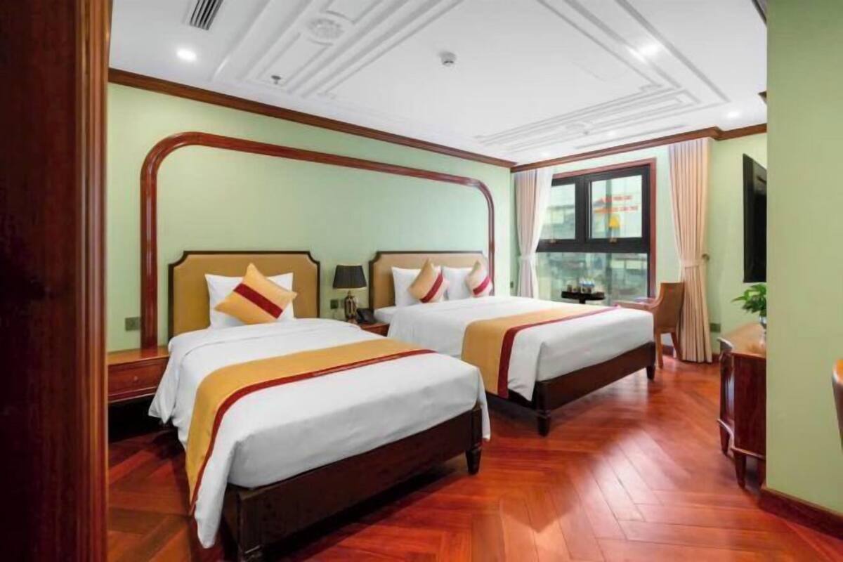 A hotel room with two beds, wooden flooring, and a large window with curtains.
