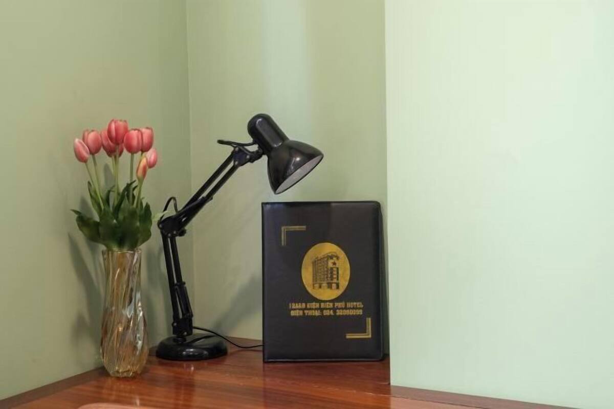 A desk with a black desk lamp, a vase with pink tulips, and a black folder with a gold emblem.