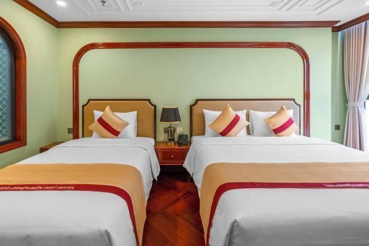 A hotel room with two beds, a nightstand, and a window with curtains.