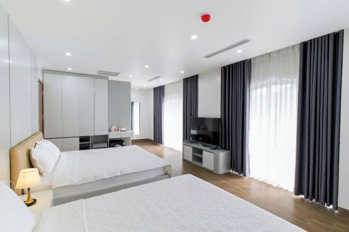 A hotel room with two beds, a TV, a desk, and a large window with curtains.