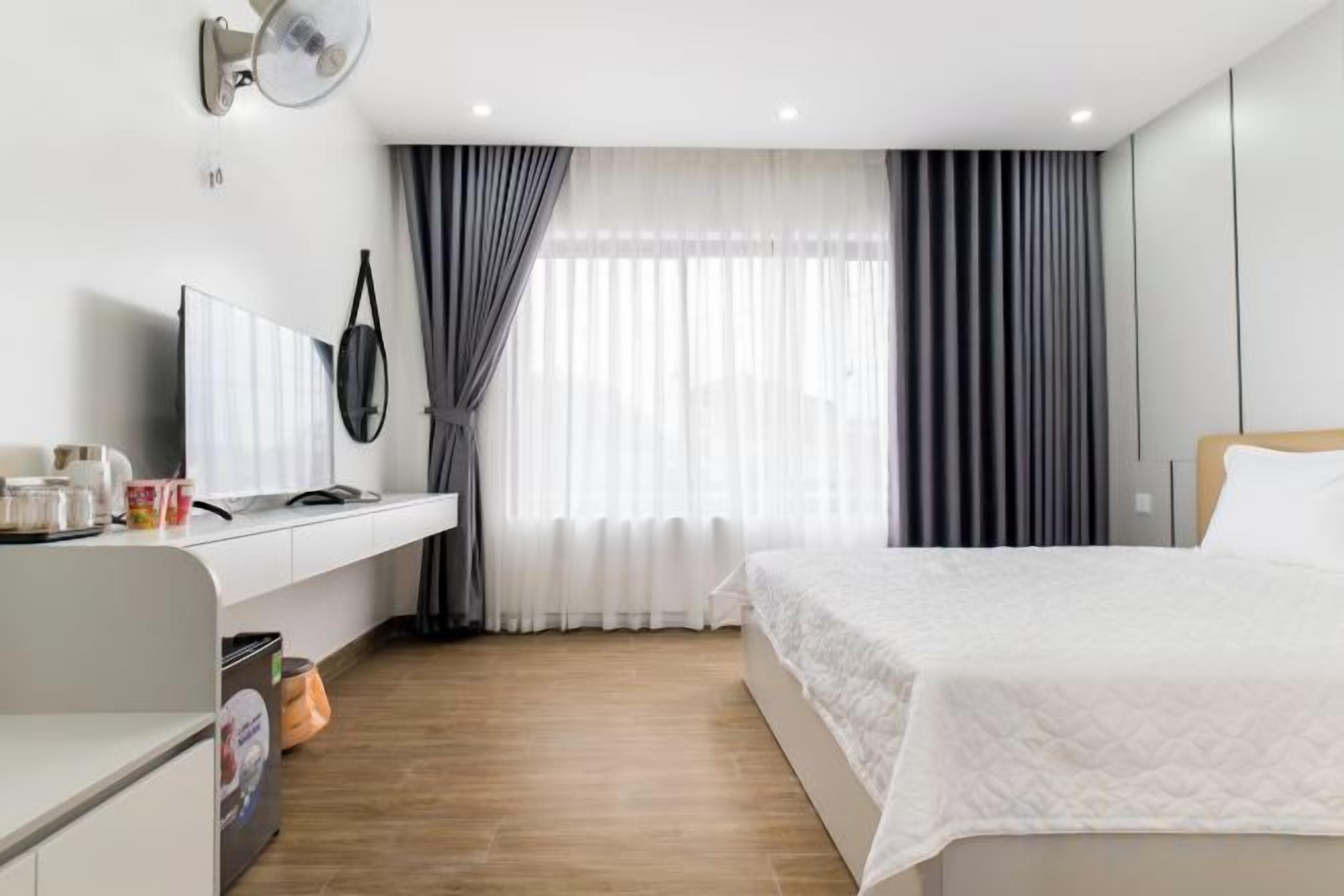 A hotel room with a bed, a desk, a television, and a window with curtains.