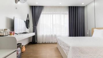 A hotel room with a bed, a desk, a television, and a window with curtains.