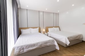 Een moderne hotelkamer met twee enkele bedden, een nachtkastje met lamp en een groot raam met gordijnen.