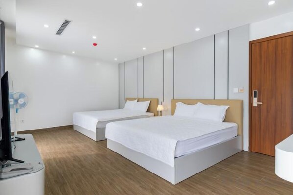 A hotel room with two beds, a wooden floor, a TV, and a wooden door. - NHAT MINH HOTEL (Lang Son)