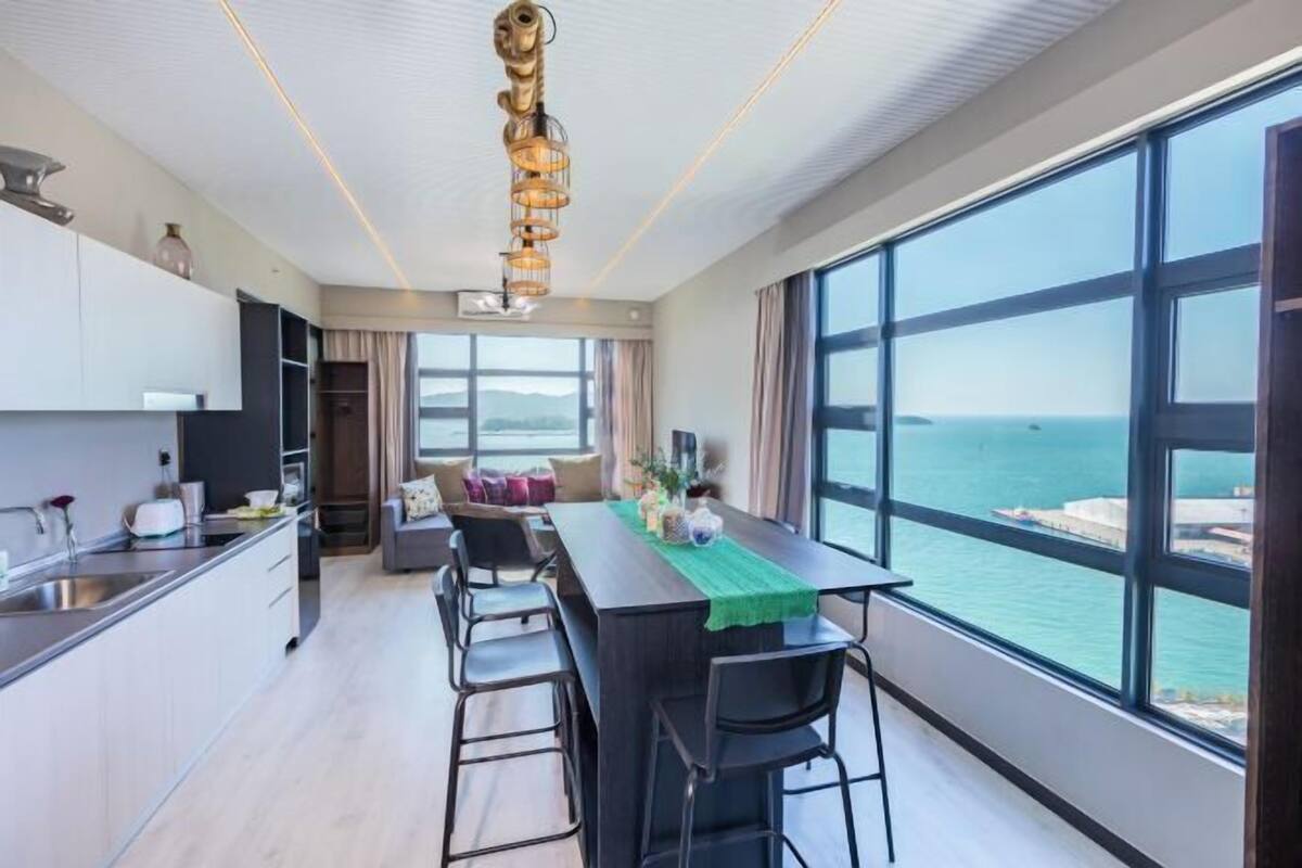 A modern kitchen with a view of the sea, a dining area with a table, and a large window.