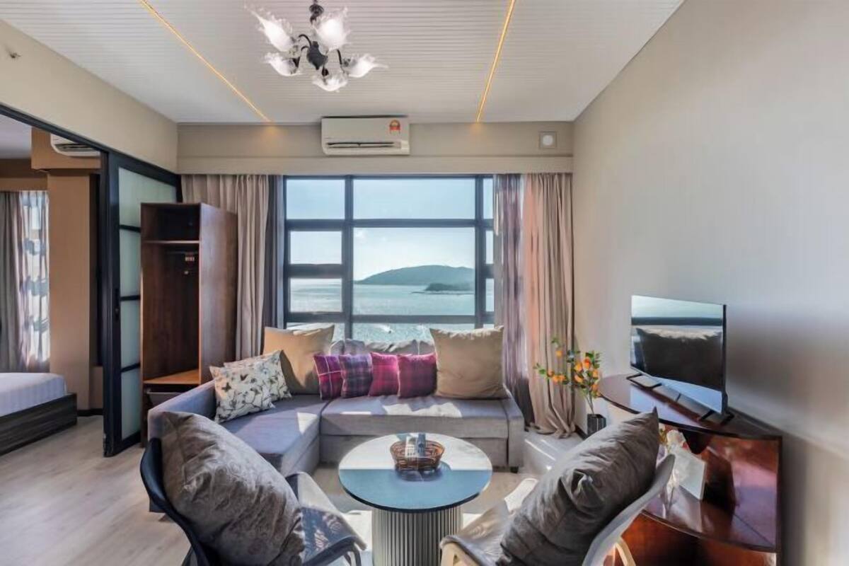 A modern living room with a sofa, television, and a view of the sea.