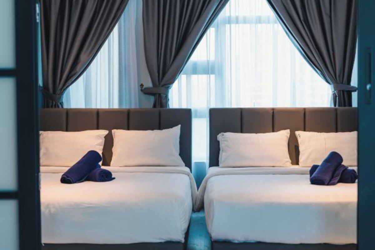 Habitación de hotel con dos camas, un ventanal con cortinas y vistas a la ciudad.