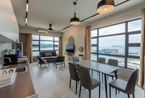 Una habitación de hotel moderna con comedor, sofá, televisión y ventanas amplias con vista al mar.