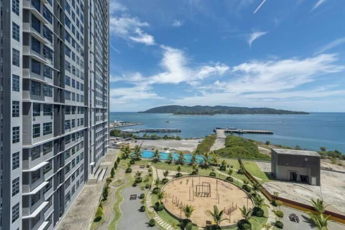 A high-rise building with a swimming pool, a circular park, and a view of the sea.