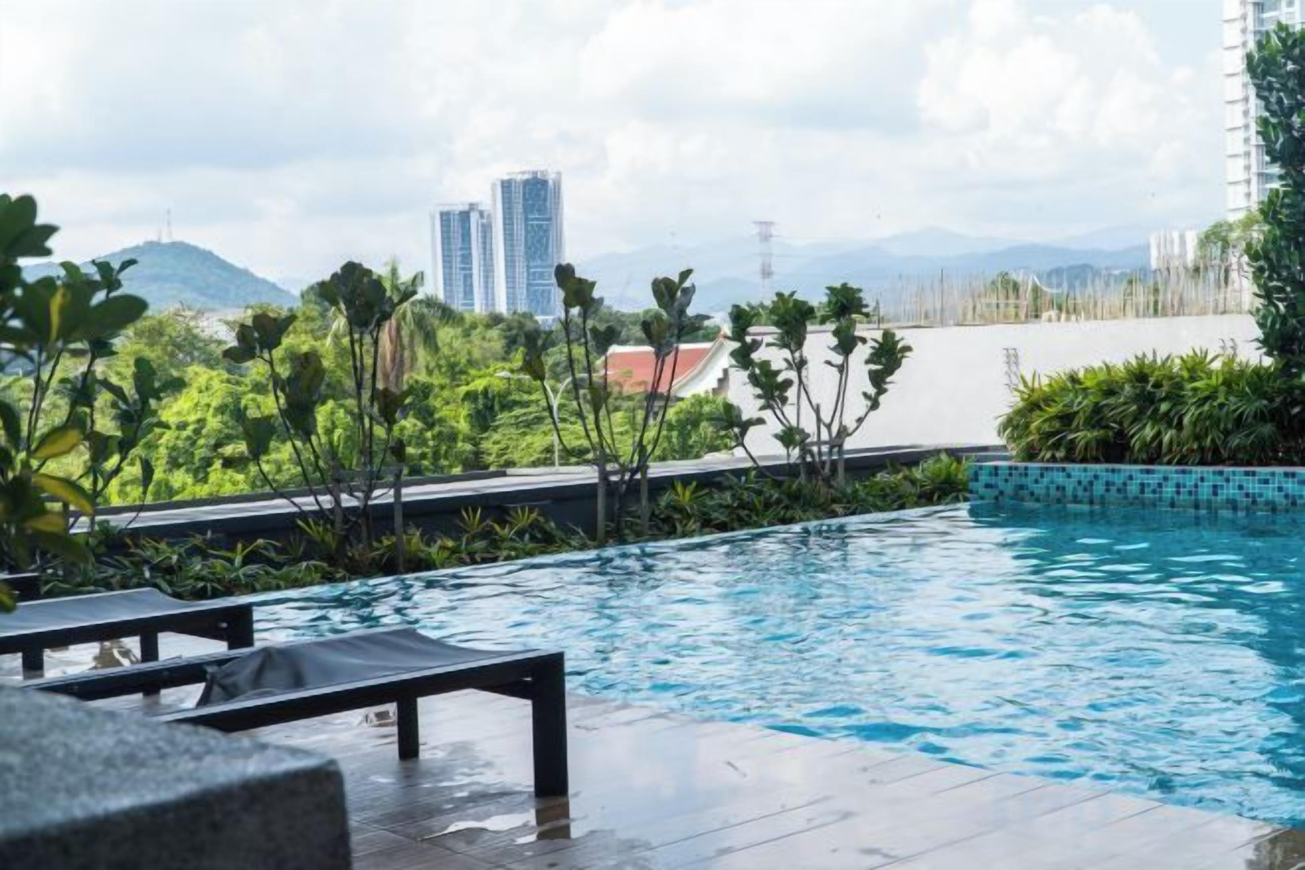 A swimming pool with lounge chairs, surrounded by greenery and buildings in the background.