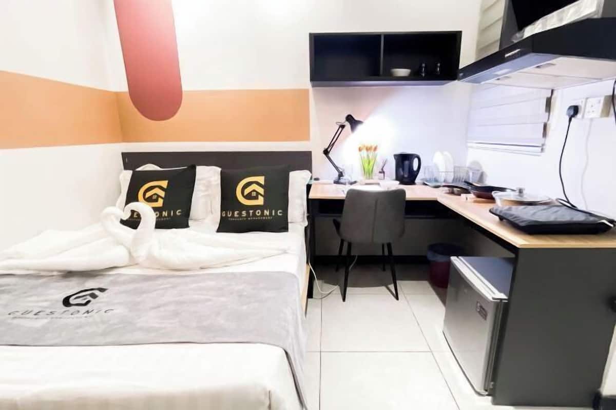 A hotel room with a bed, a desk, a chair, a lamp, and a small refrigerator.
