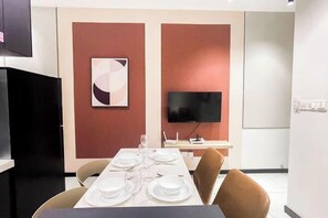 A dining area with a table set for four, a flat-screen TV, and a whiteboard on the wall.