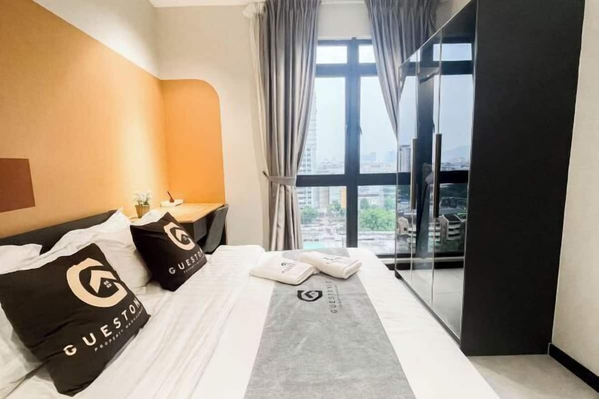 A hotel room with a bed, a nightstand, a window with curtains, and a view of the city.