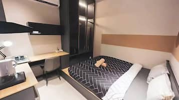 A modern hotel room with a bed, desk, chair, and a wardrobe.