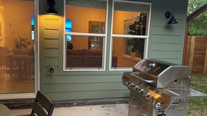 Een terras met een barbecue, een tafel en stoelen.