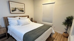 Een slaapkamer met een bed, een nachtkastje, een plafondventilator, een raam met jaloezieën en een kamerplant.