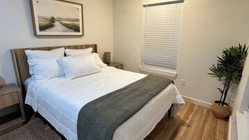A bedroom with a bed, a nightstand, a ceiling fan, a window with blinds, and a potted plant.