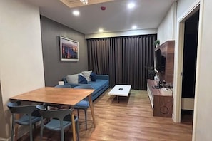 Un espace de vie compact comprenant un canapé, une table à manger avec des chaises, une petite table basse et un téléviseur posé sur un meuble en bois.