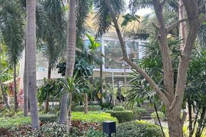 A landscaped garden with palm trees and various plants, a modern building in the background, and a clear sky. - Dusit Grand Park Resort Apartment Pattaya (Pattaya)