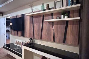 A modern kitchen with a black countertop, wooden wall panels, and a shelf with decorative items. - Dusit Grand Park Resort Apartment Pattaya (Pattaya)