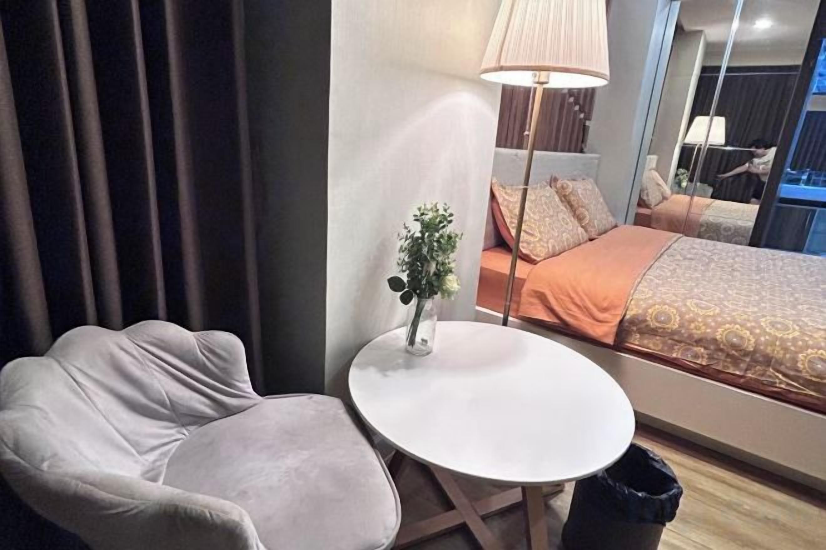 Hotellihuone, jossa on sänky, pyöreä pöytä, tuoli, lamppu ja pieni kasvi.