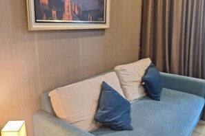 A light blue sofa with two pillows, a framed picture on the wall, and a lamp on the left. - Dusit Grand Park Resort Apartment Pattaya (Pattaya)
