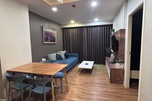 A living room with a wooden dining table, blue sofa, and a TV on a wooden stand.