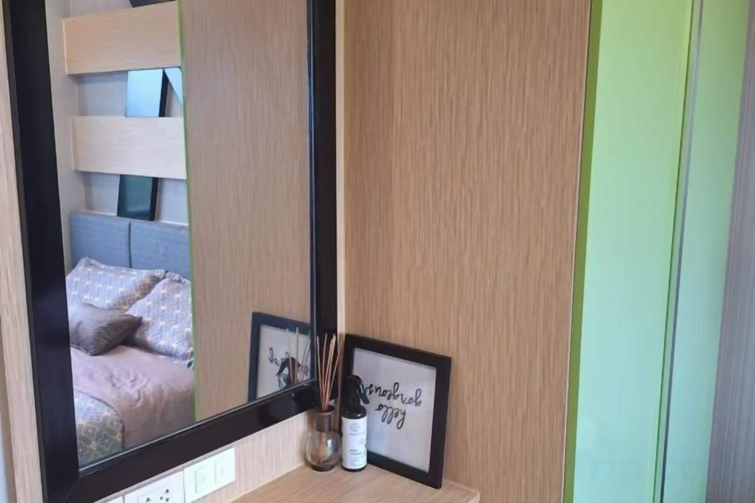 Un dormitorio con un espejo grande, una mesita de noche con un cuadro enmarcado y un pequeño florero con una vela.