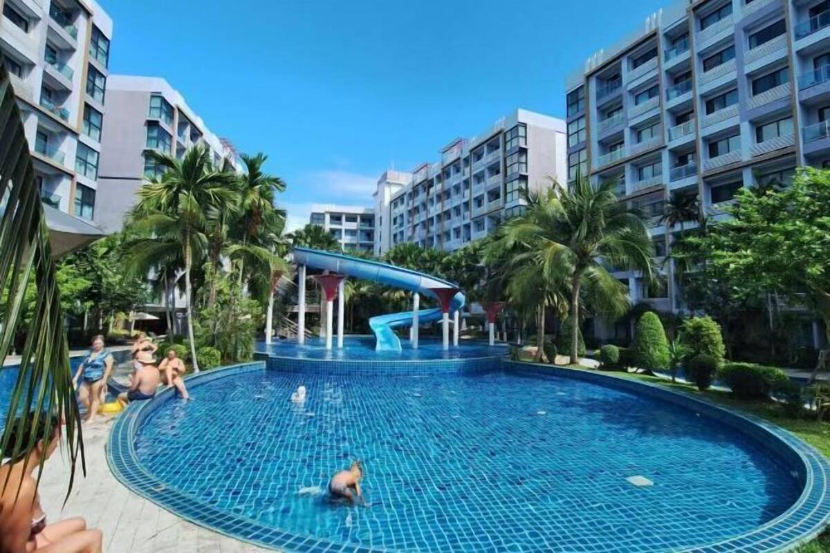 Ein Swimmingpool mit Wasserrutsche, umgeben von Palmen und modernen Gebäuden.