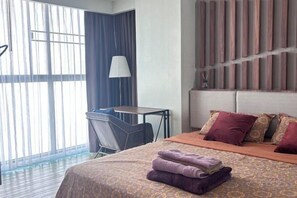 Une chambre d’hôtel avec un lit, un bureau, une chaise et une grande fenêtre.
