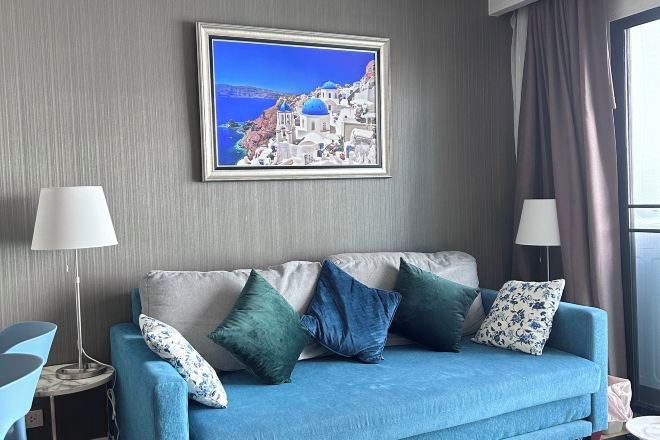 Een kamer met een blauwe bank, twee bijzettafels, een ingelijst foto aan de muur en een raam met gordijnen.