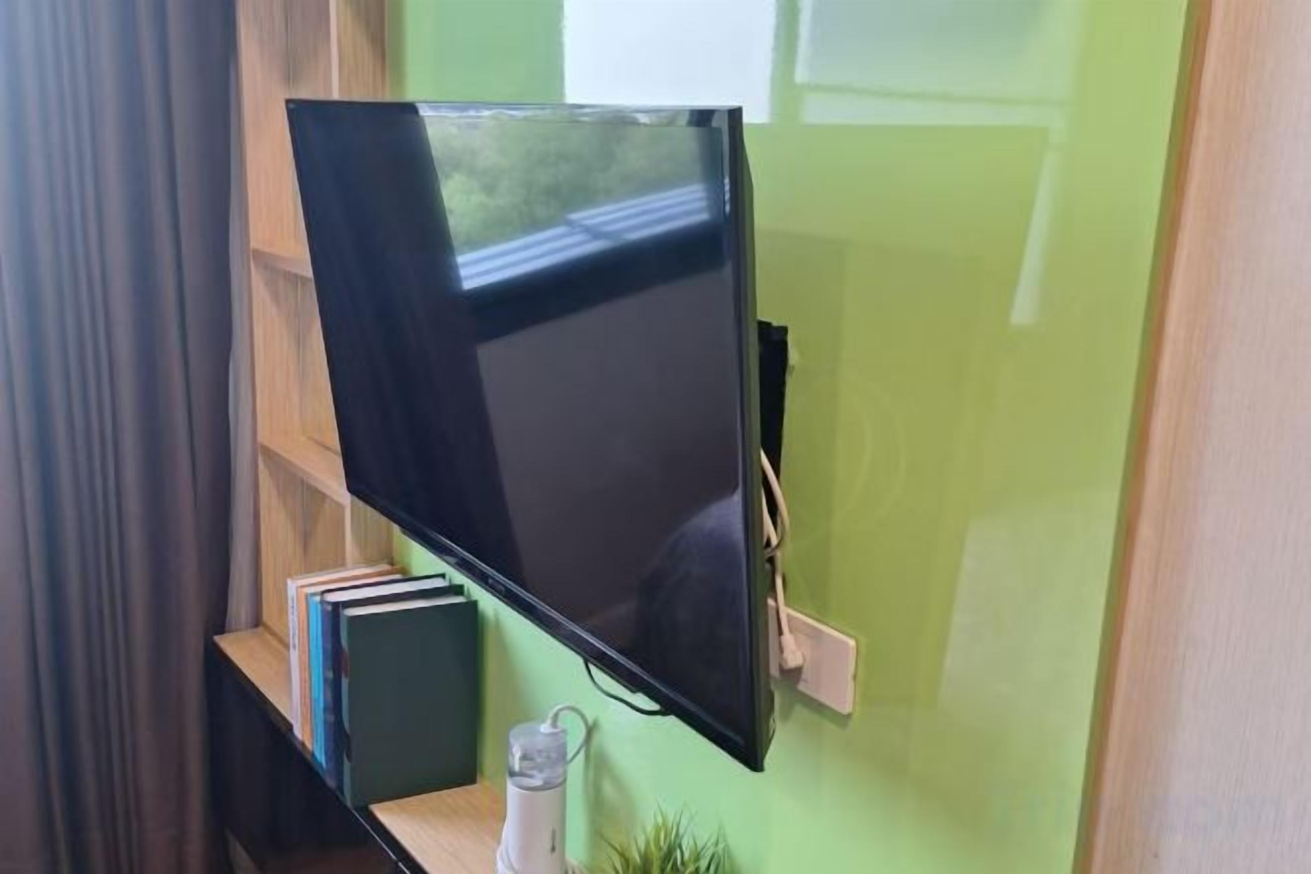A flat-screen TV mounted on a wall, with a shelf below holding books and a small plant.