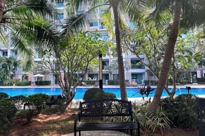 Un espace aménagé au bord de la piscine, avec un banc, des palmiers et un bâtiment en arrière-plan.