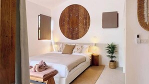 A modern bedroom with a large bed, bedside tables, a wall-mounted circular artwork, and a potted plant. - Villa Lucky, Villa 13 (Koh Samui)