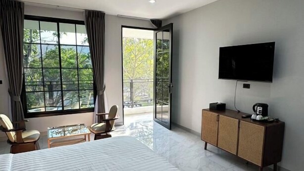 A hotel room with a large bed, a TV, a small table, two chairs, a cabinet, and a balcony with a view. - Bamboo Resort (Si Prachan)
