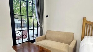 A room with a wooden table, a beige sofa, and a bed with a white bedspread. - Bamboo Resort (Si Prachan)