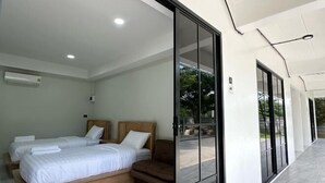 A modern hotel room with two beds, a sofa, and a large sliding glass door leading to an outdoor area. - Bamboo Resort (Si Prachan)
