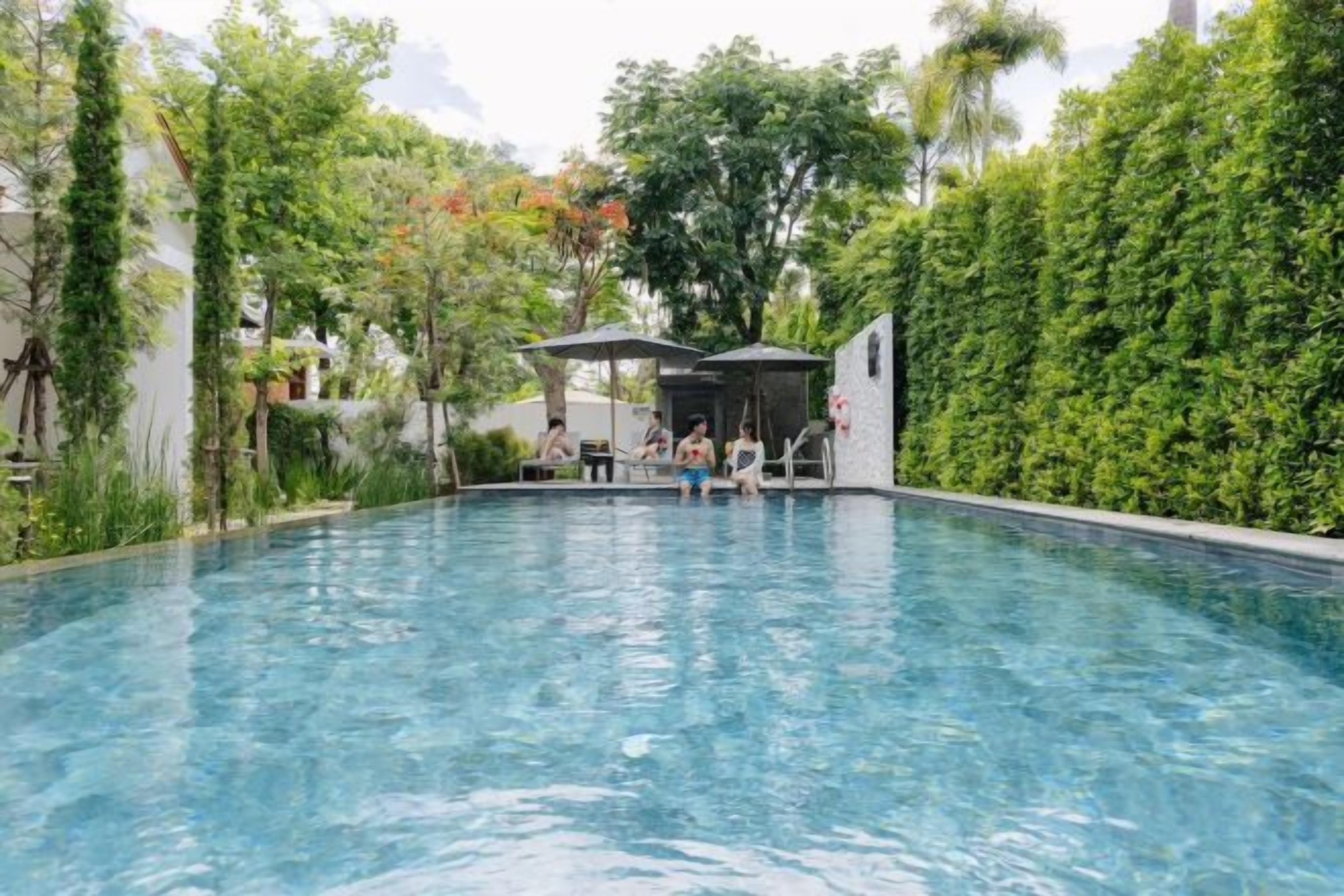 A swimming pool with a seating area and umbrellas, surrounded by greenery.